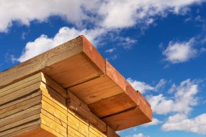 A close-up of stacked lumber with a blue sky and clouds in the background