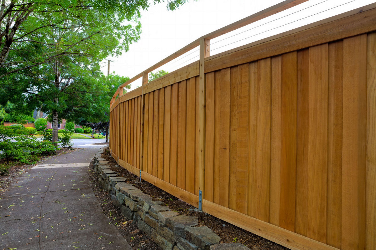 A wood fence near a concrete pathway and trees.